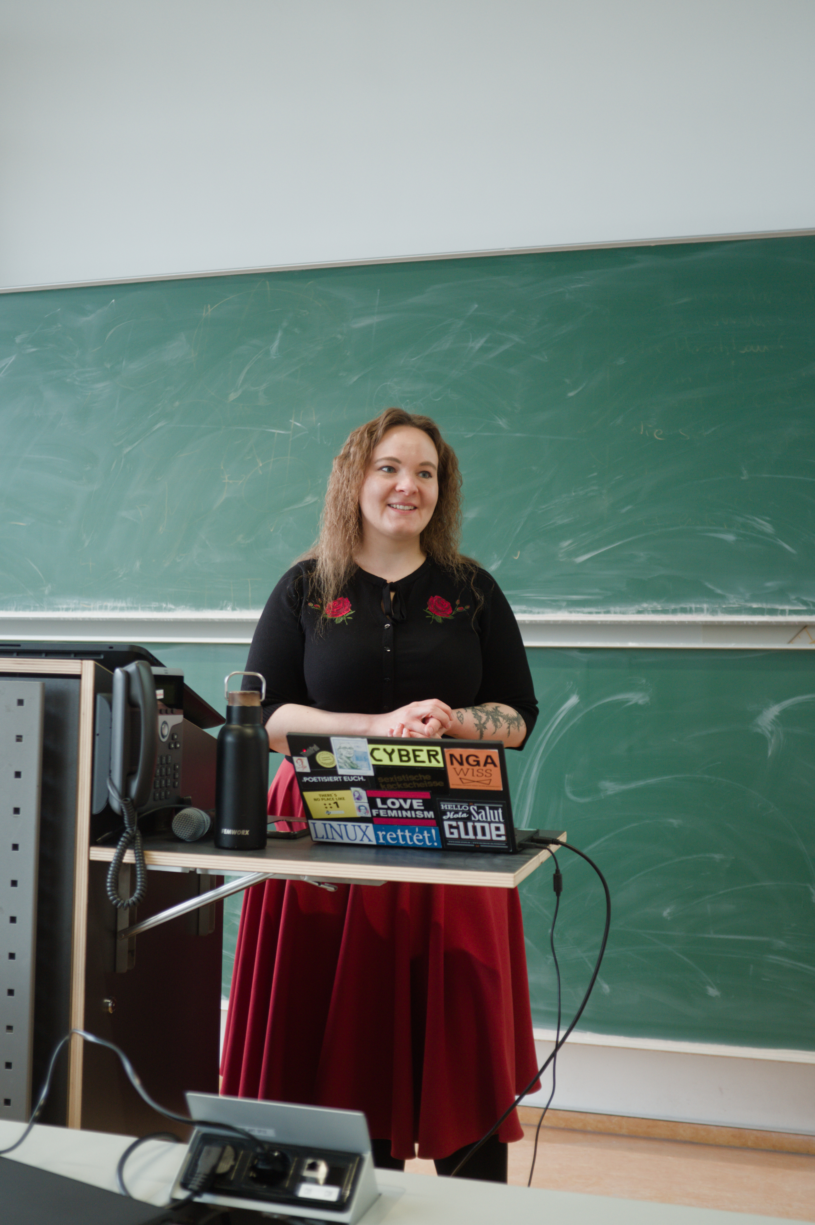 Lea steht vor einem mit bunten Stickern beklebtem Laptop am Präsentationstisch.