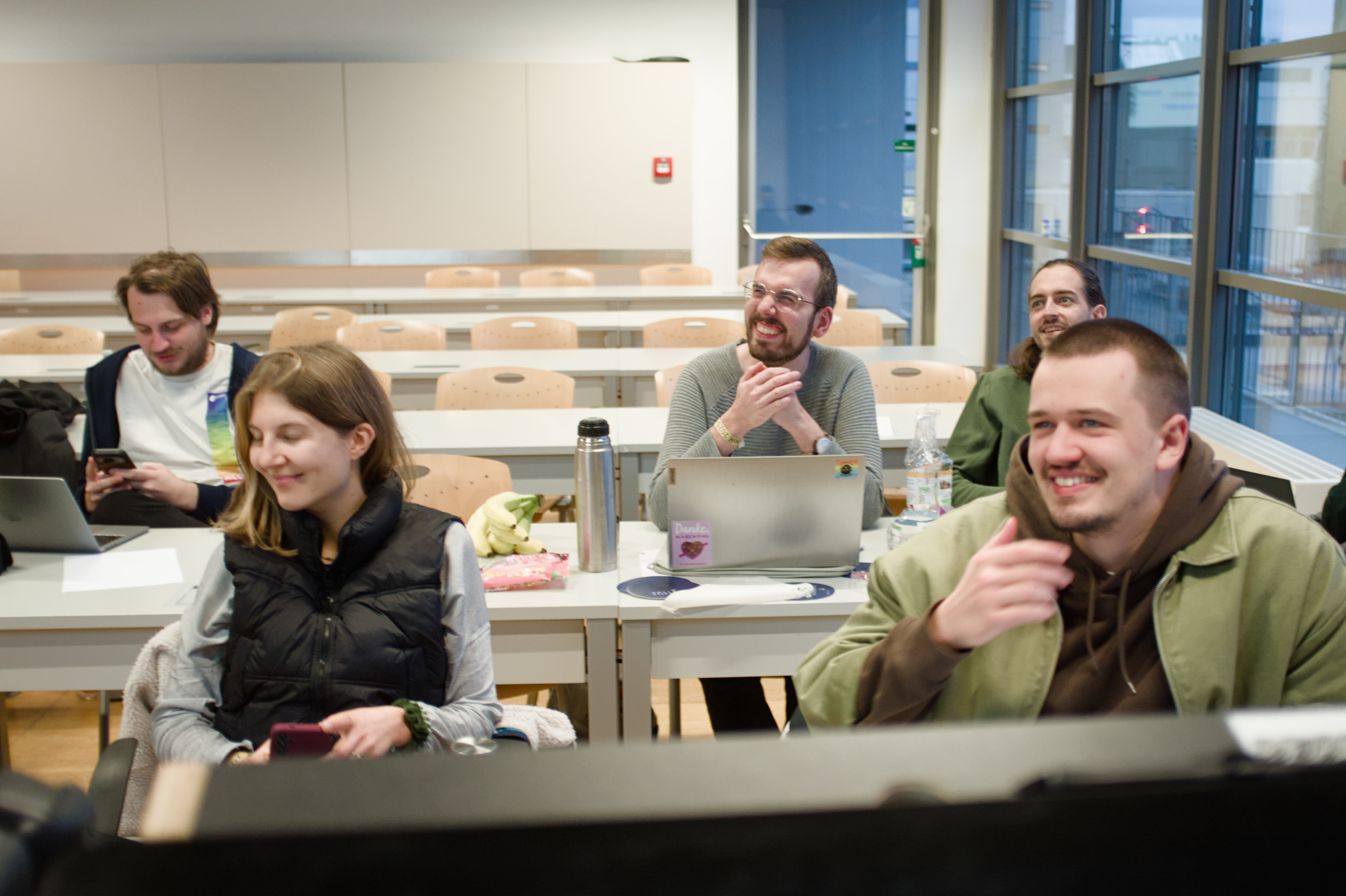 Eine Gruppe von Personen sitzt zusammen an den Unibänken. Das Bild ist verwackelt weil alle sich lachen bewegen.